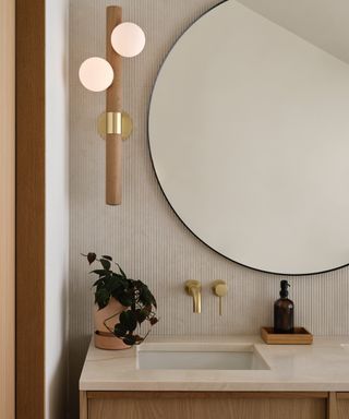 Neutral elegant bathroom with round mirror, wood and marble style vanity, textured tiles, wood and brass wall light,