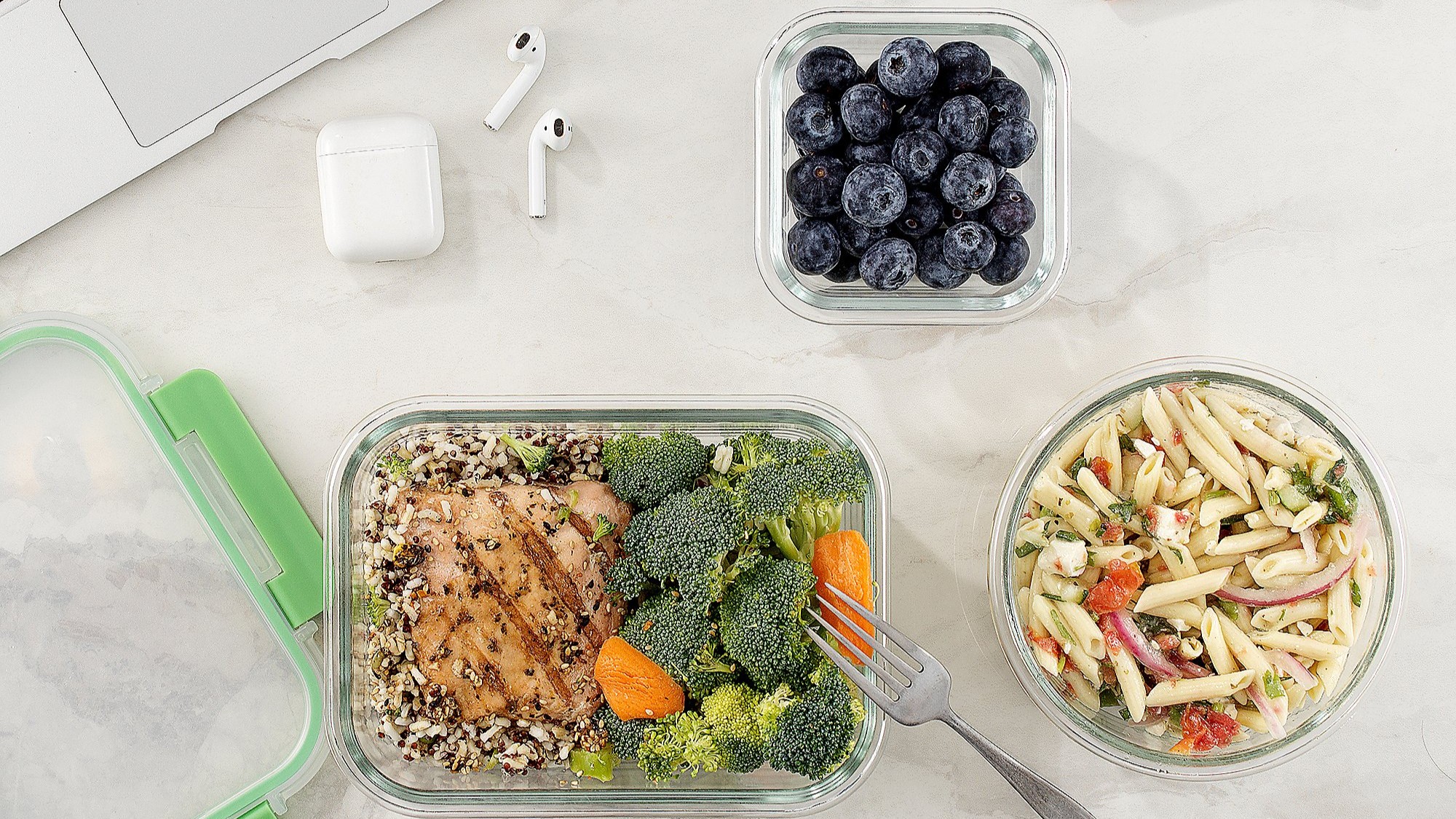 A lunch of chicken and rice, with broccoli, pasta salad and blueberries in food storage containers.