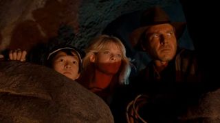 From left to right: Ke Huy Quan, Kate Capshaw, and Harrison Ford peeking out from a cave in Indiana Jones and the Temple of Doom. 