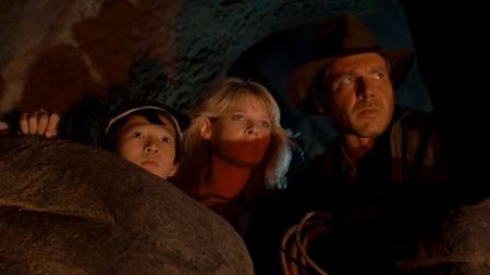 From left to right: Ke Huy Quan, Kate Capshaw, and Harrison Ford peeking out from a cave in Indiana Jones and the Temple of Doom. 
