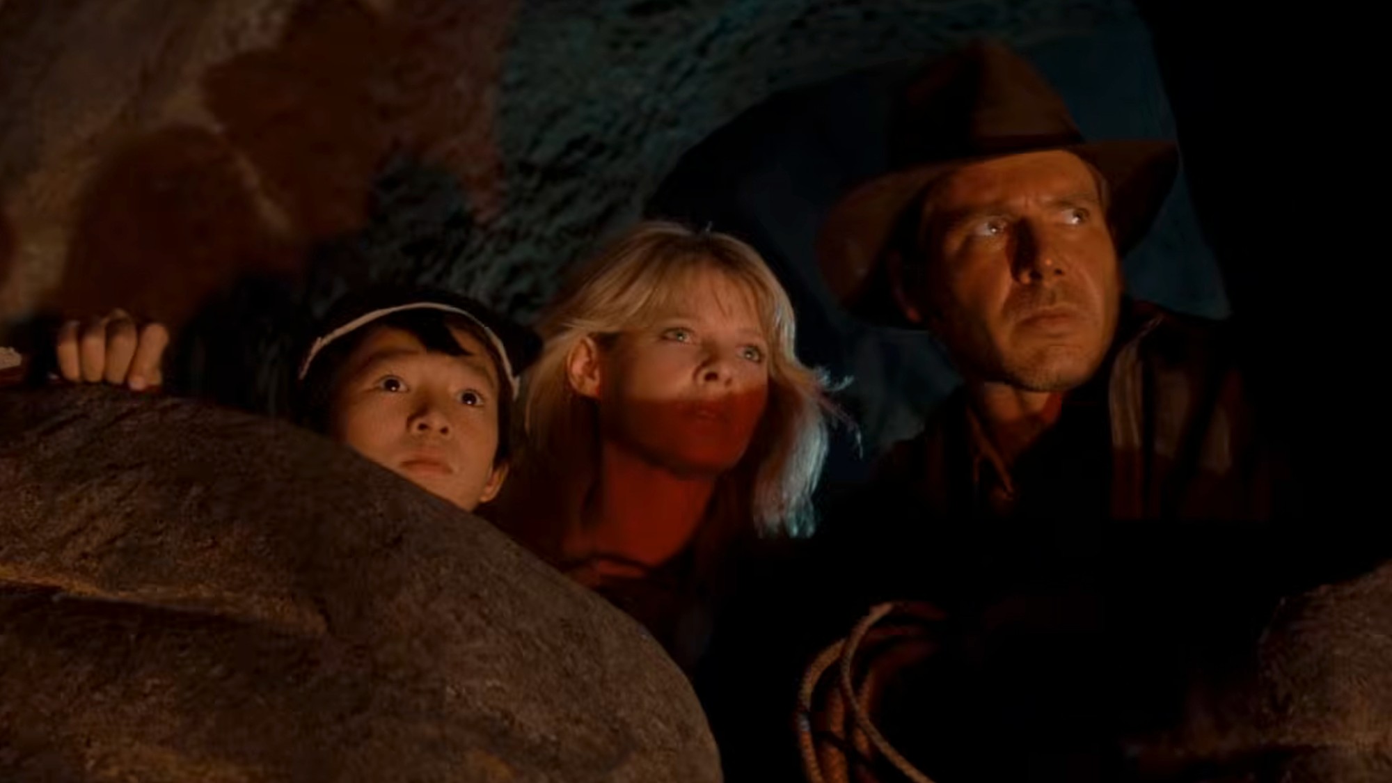 From left to right: Ke Huy Quan, Kate Capshaw, and Harrison Ford peeking out from a cave in Indiana Jones and the Temple of Doom. 