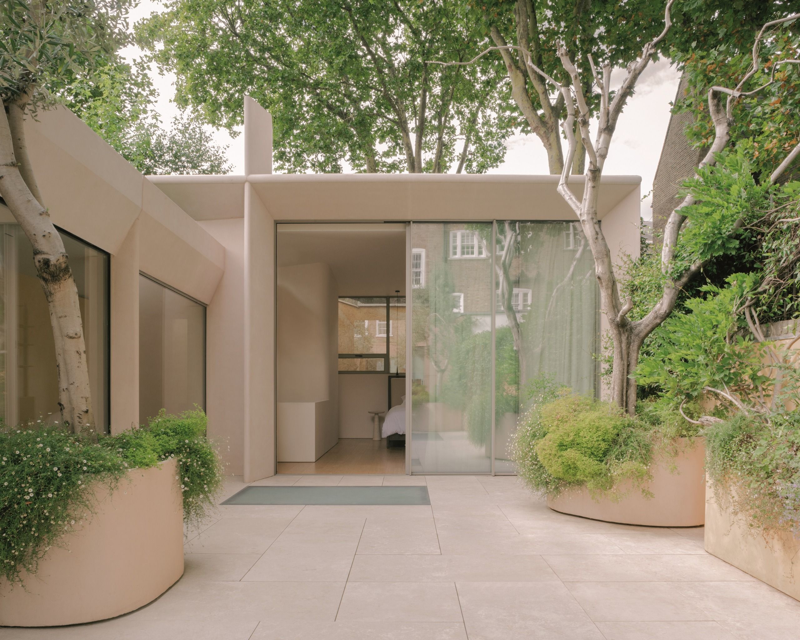 modern extension with rendered exterior and glass sliding doors with planters around trees