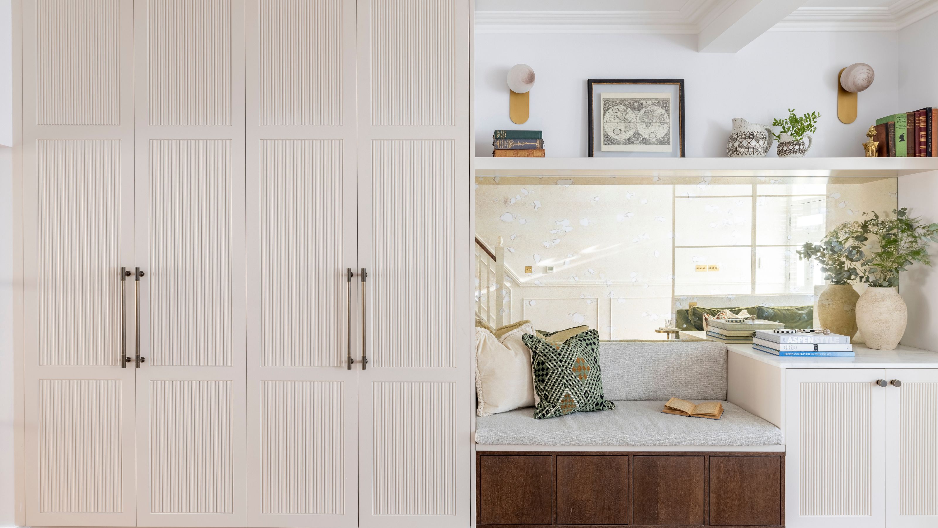 A mudroom in a home with a bench seating area as well as open shelving above the seating area with books and a framed piece of art