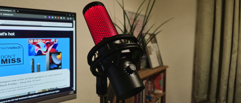 The HyperX Quadcast 2 in an office on a mic arm in front of a PC screen and a bookshelf