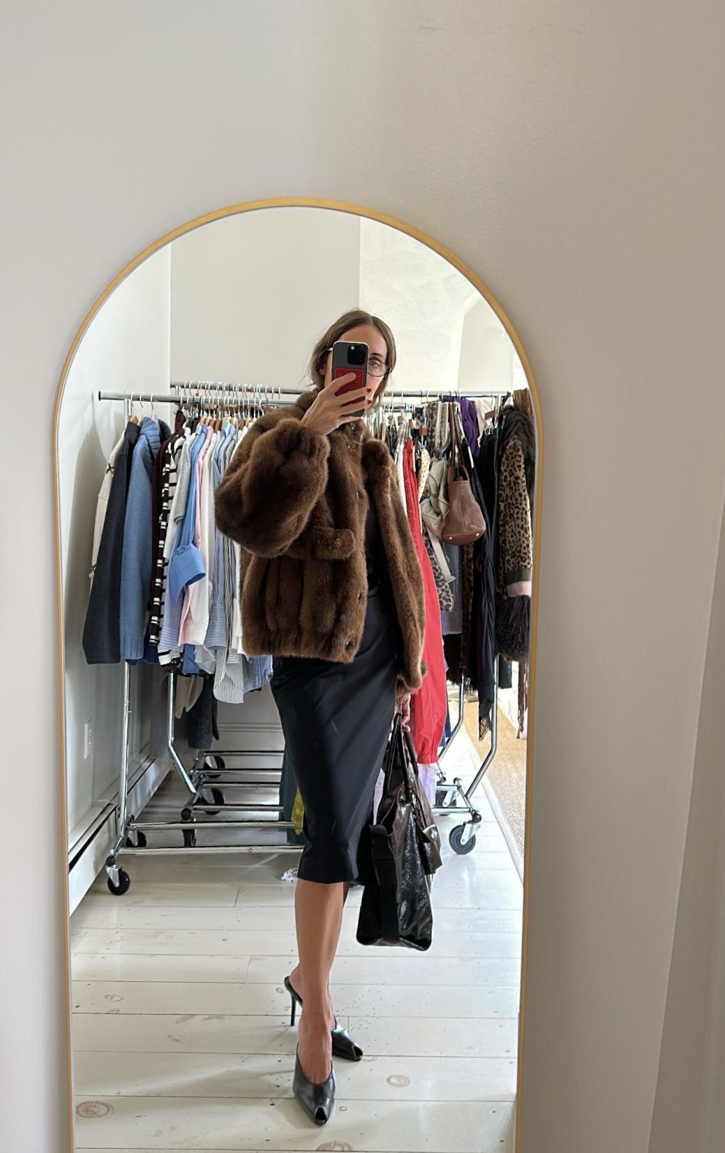 Larissa Mills wearing a black dress, brown fur coat, black leather tote bag, black heels, posing in a mirror selfie.