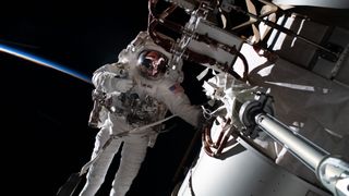 astronaut in a spacesuit with the horizon of earth's atmosphere in behind. a part of the space station is visible at right