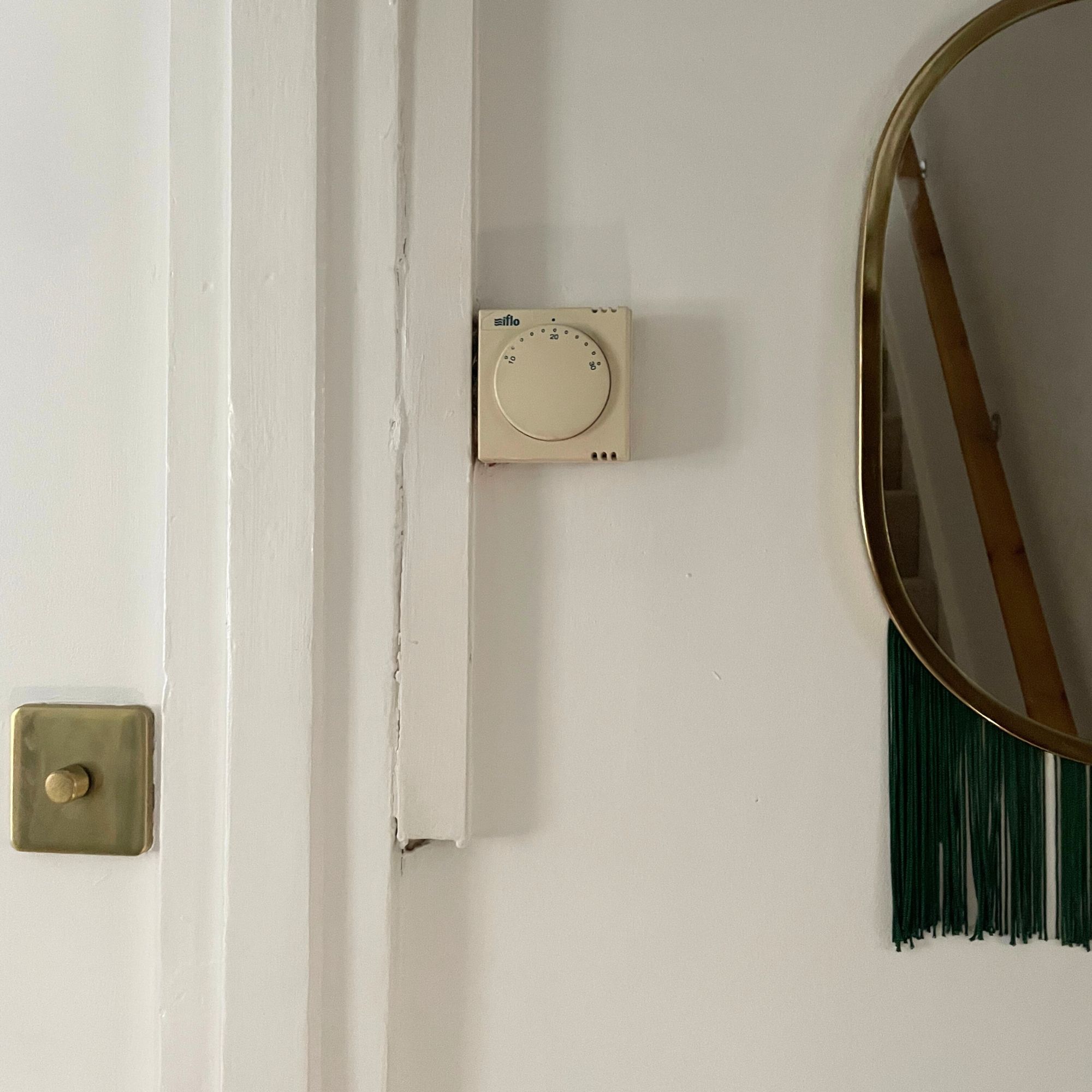 Old thermostat on a white painted wall, next to a lightswitch and a mirror