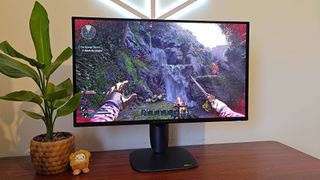 Alienware AW2725Q monitor with Avowed gameplay on screen featuring character holding dagger in front of waterfall