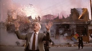 A still shot from The Naked Gun, showing actor Leslie Nielsen holding up his hands and saying 'Nothing to see here' in front of a burning building.