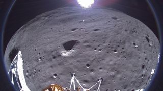 a fisheye photo showing parts of a gold and silver lunar lander in the foreground, with the moon's gray dirt and the bright sun in the background.