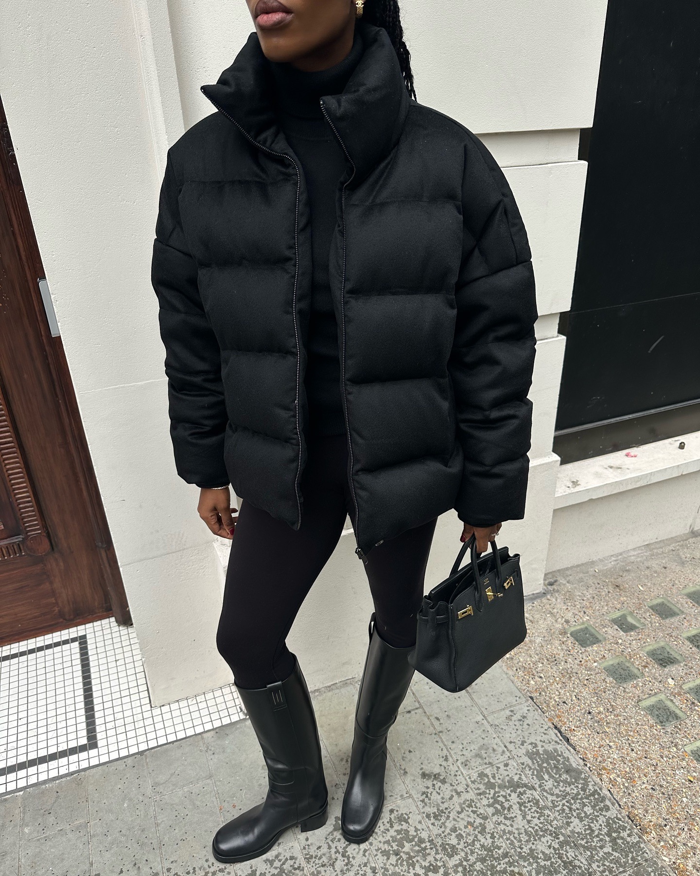 Influencer wears a black puffer jacket with black leggings and black knee-high boots.