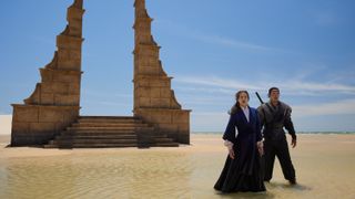 Moiraine (Rosamund Pike) and Lan (Daniel Henney) standing on a blue sky beach in front of a waygate in The Wheel of Time season 2 episode 8