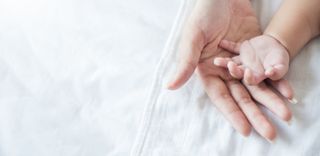 A baby's hand resting on a mother's hand.