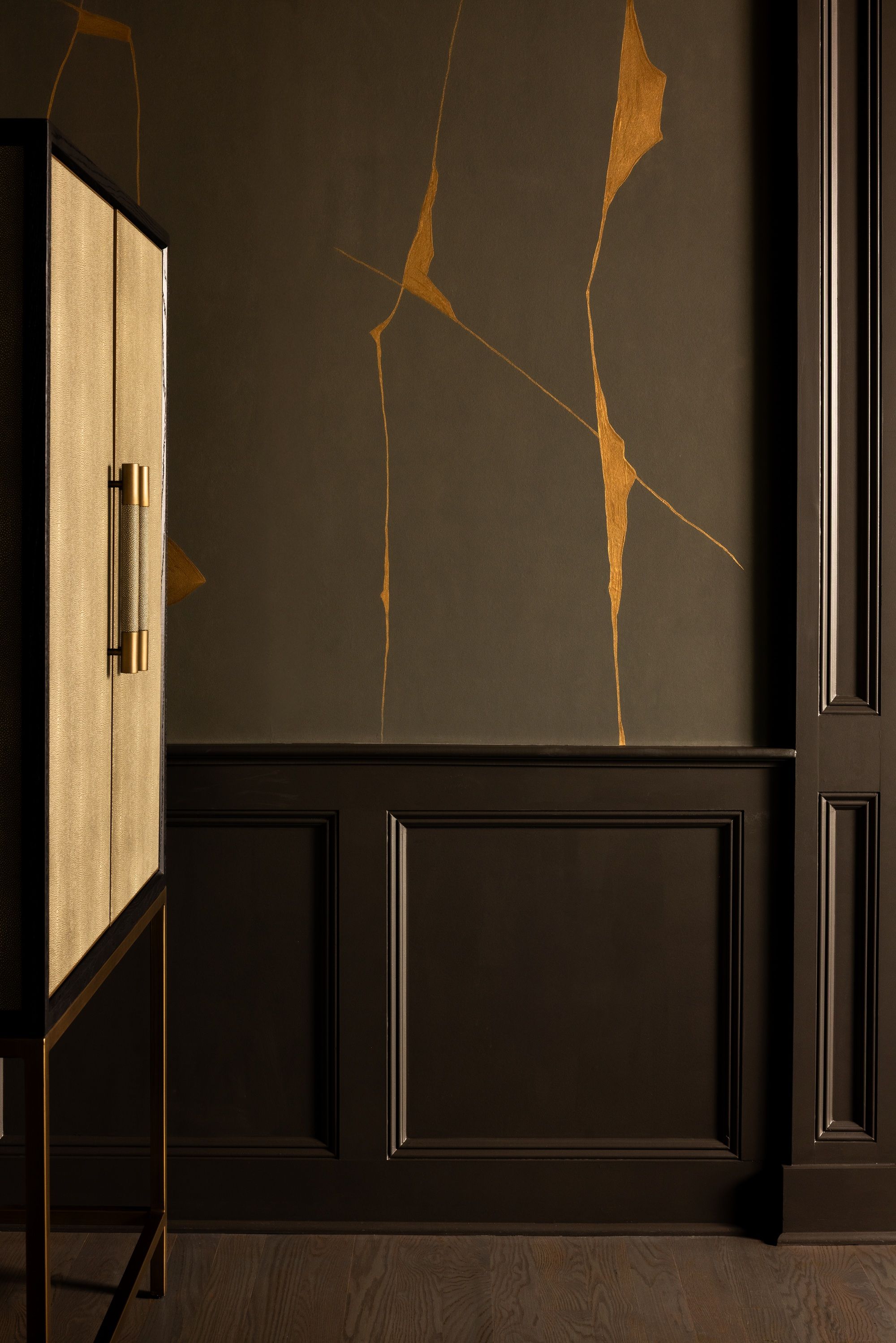 a wall with kintsugi wallpaper and paneling in dark colors