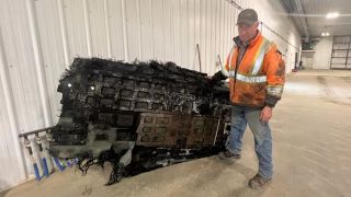 a person standing beside a very large piece of debris. the debris is charred and roughly the same width as a person's height