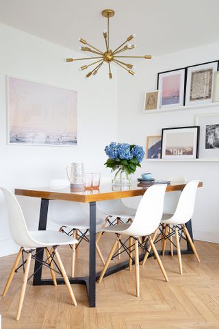 A Scandi-style dining space with white walls, parquet flooring, white Eames-style chairs and an industrial wood dining table with thick metal legs