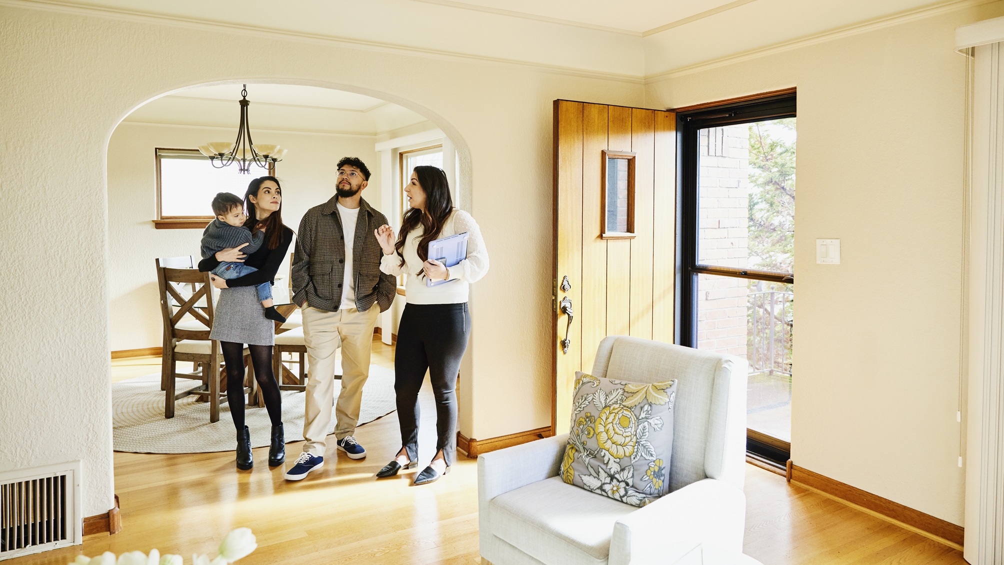 A couple with a small child look at a home for sale with a real estate agent.