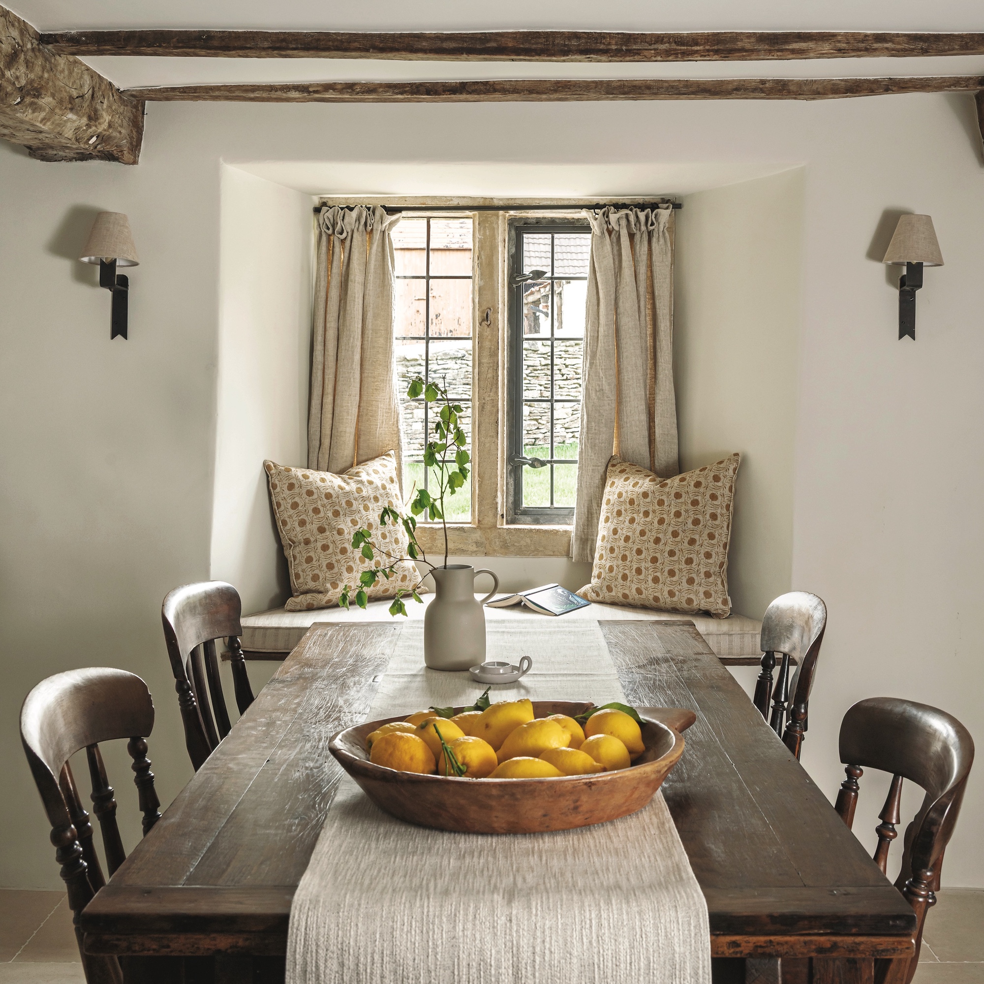 cottage dining room with farmhouse wooden table and wooden chairs in front of stone mullion window with window seat