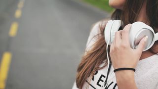 Best podcasts: A woman wearing a pair of white over-ear headphones round her neck