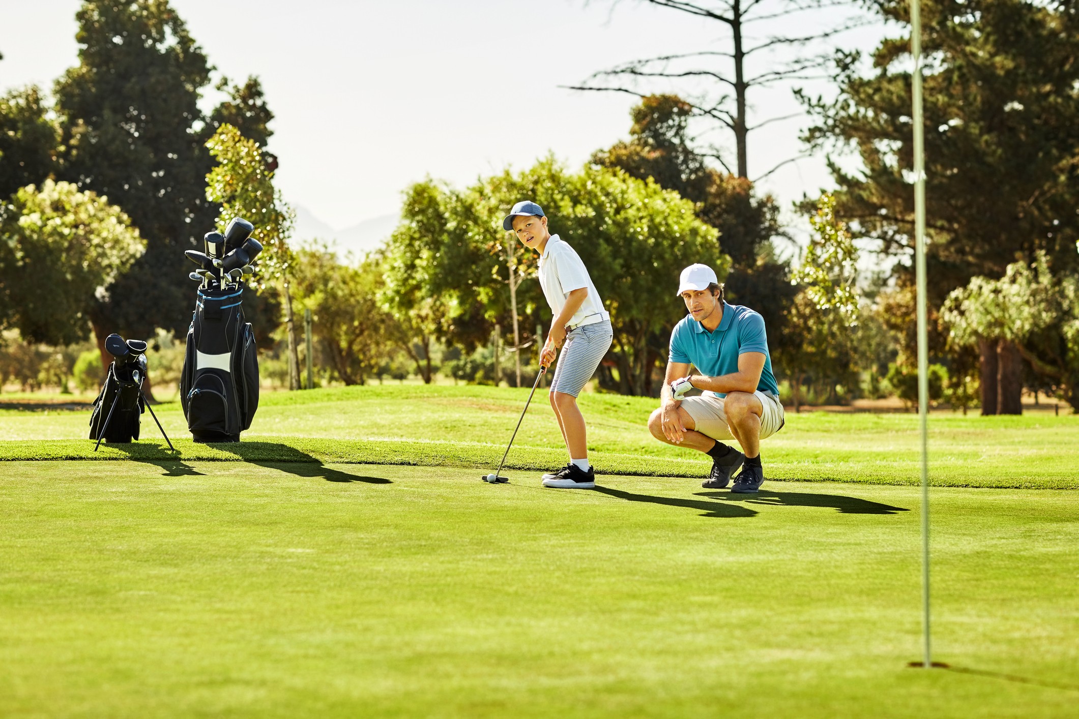 A boy putting with an adult crouched down beside him as if having just given advice