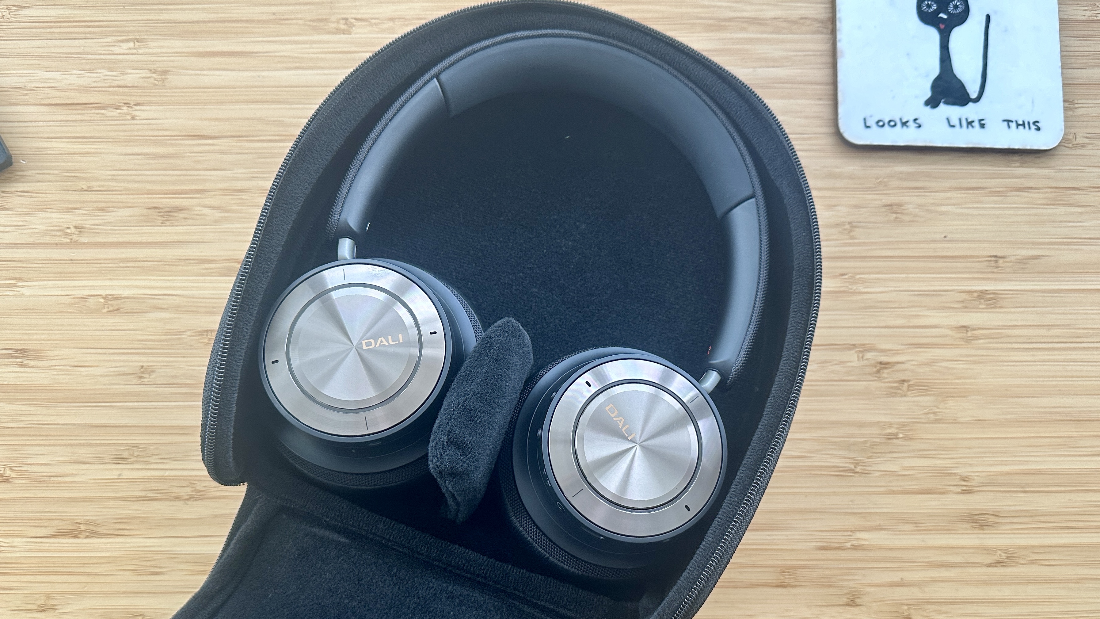 Dali IO-8 over-ear headphones, in their carry case, on a wood surface