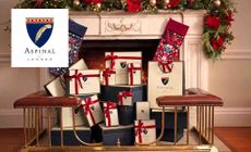 Aspinal of London logo placed over an image of aspinal gift bags in a christmas themed fireplace 