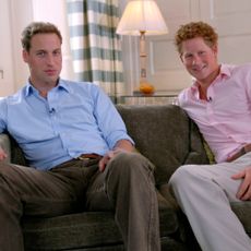 Princes William and Harry pose together on a couch wearing shirts and slacks