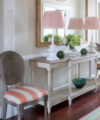 Small hallway ideas illustrated by a console table with symmetrical lamps either side of a gilt mirror.