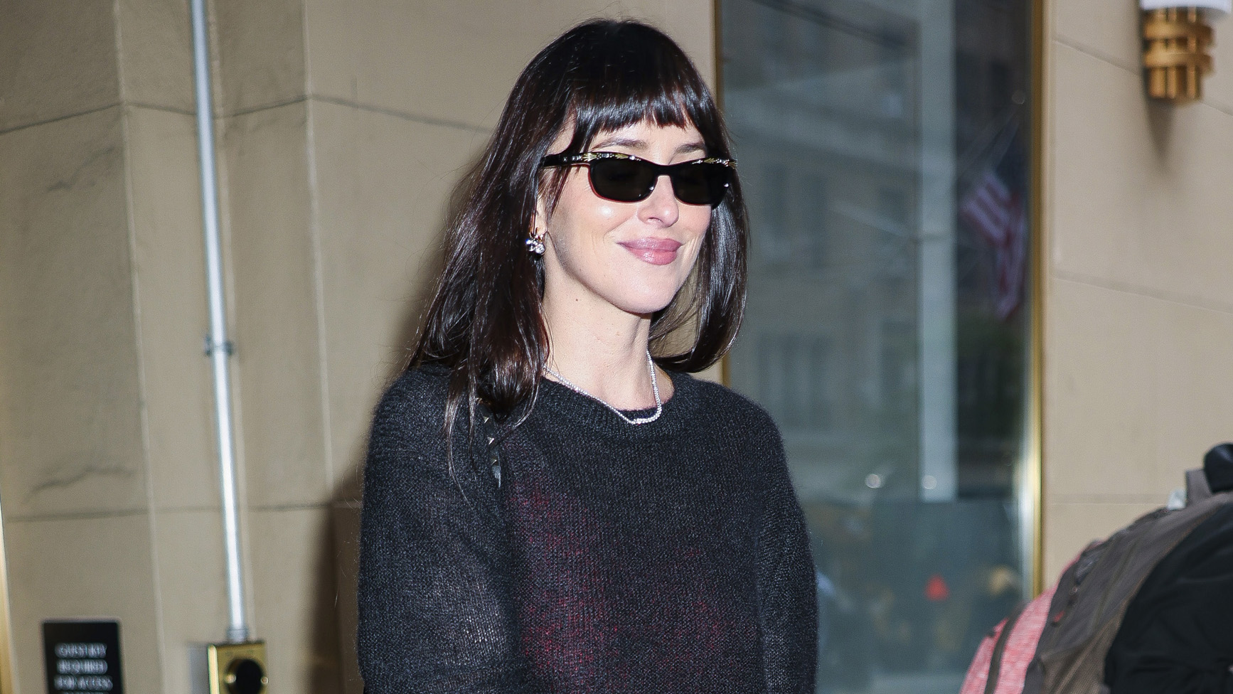 Dakota Johnson wearing a sheer black sweater, maxi skirt, and cream pointed-toe glove pumps in NYC.
