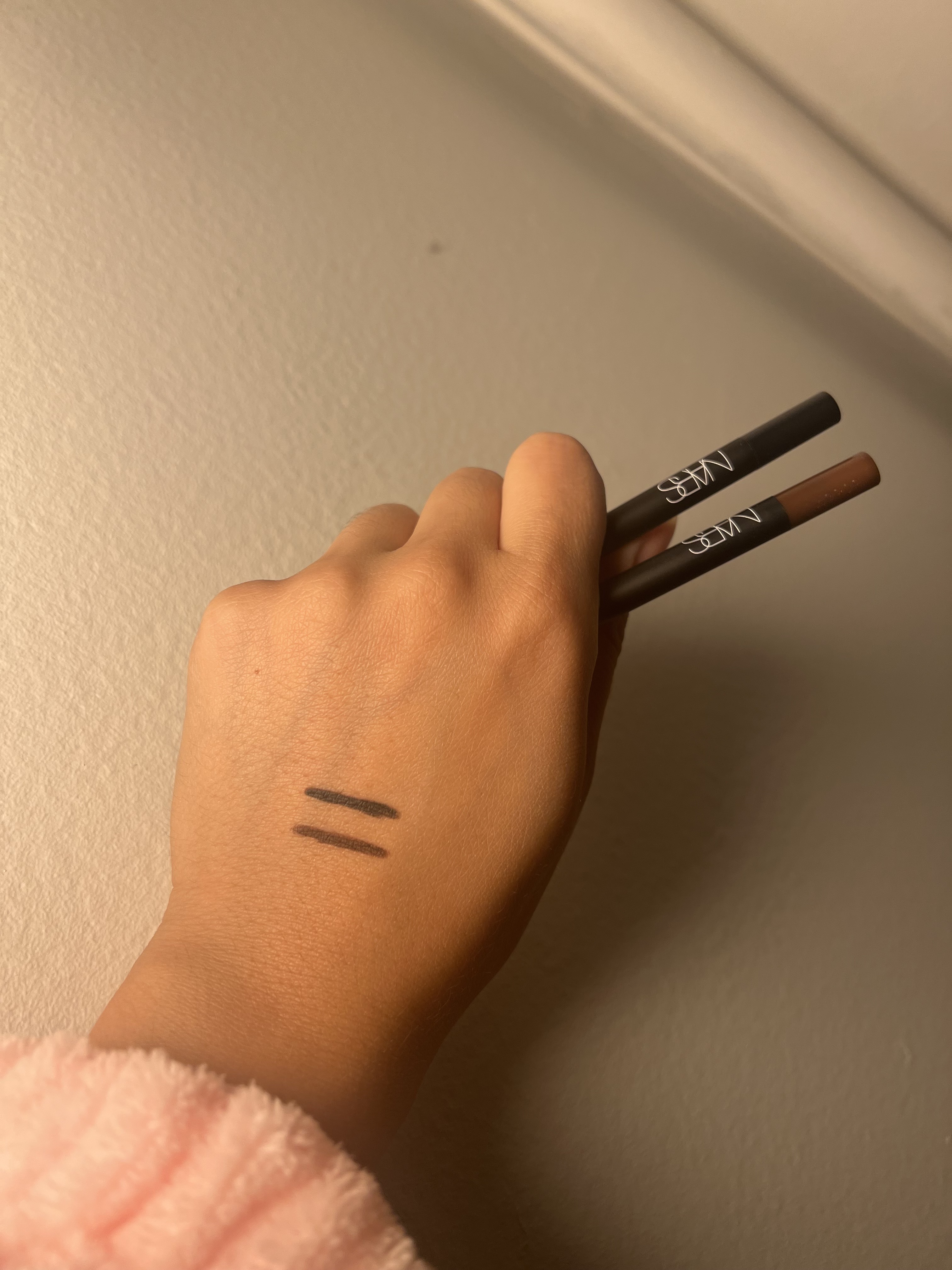 NARS High-Pigment Longwear Eyeliner black and brown swatches on back of hand holding nars eyeliner pencils