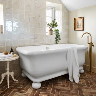 bathroom with a large traditional bath tub, with brushed brass mixer, terracotta floor tiles and small side table