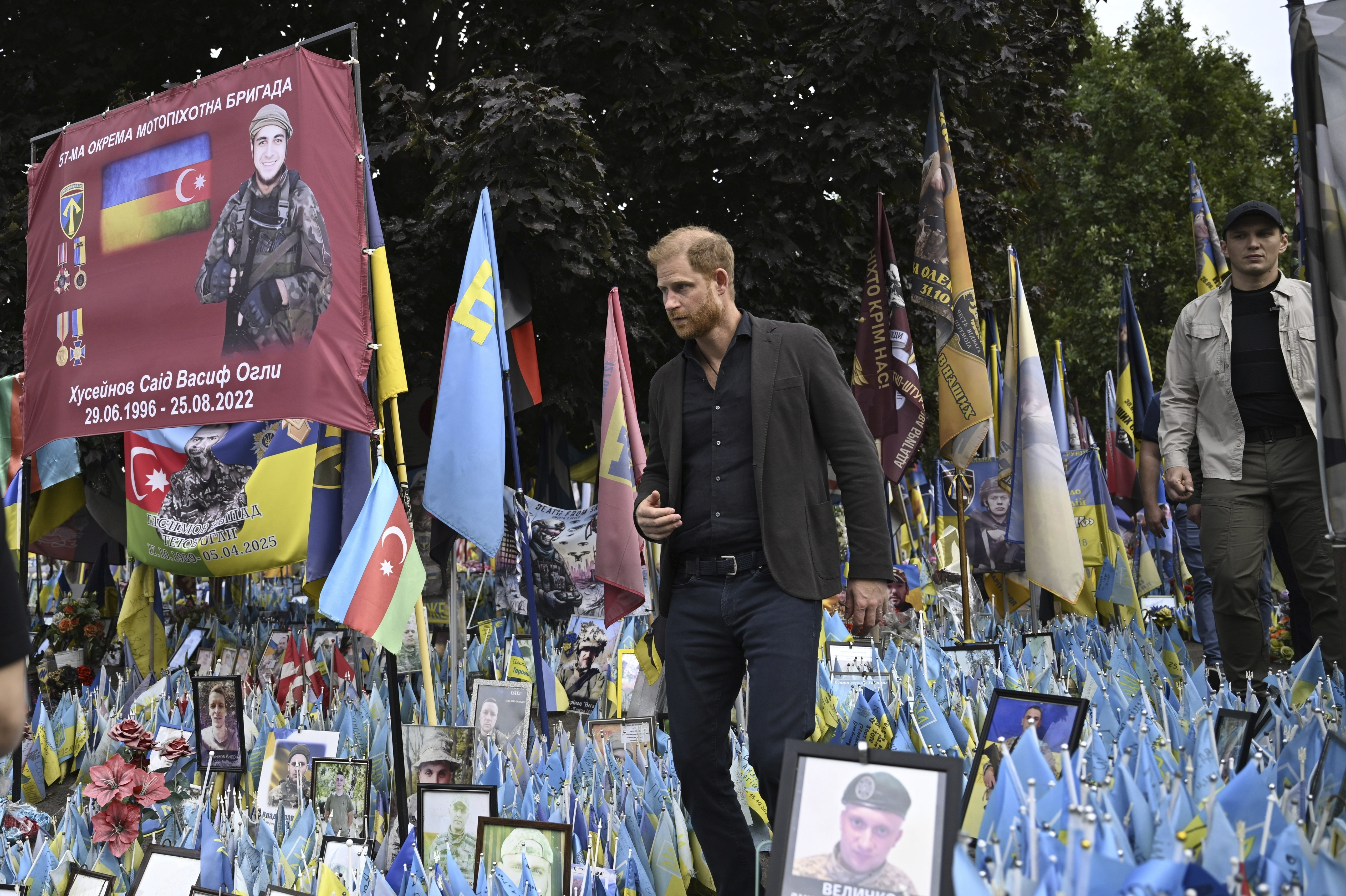 Prince harry wearing a dark suit walking through a memorial of flags and photos in Kyiv