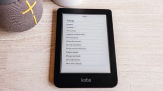 The Kobo Clara 2E laying flat on a table next to a speaker showing it's settings.