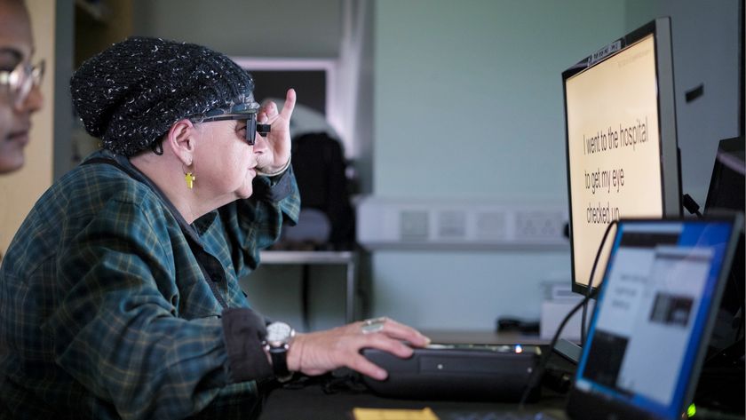 a photo of an older woman wearing augmented-reality glasses to read words on a computer screen