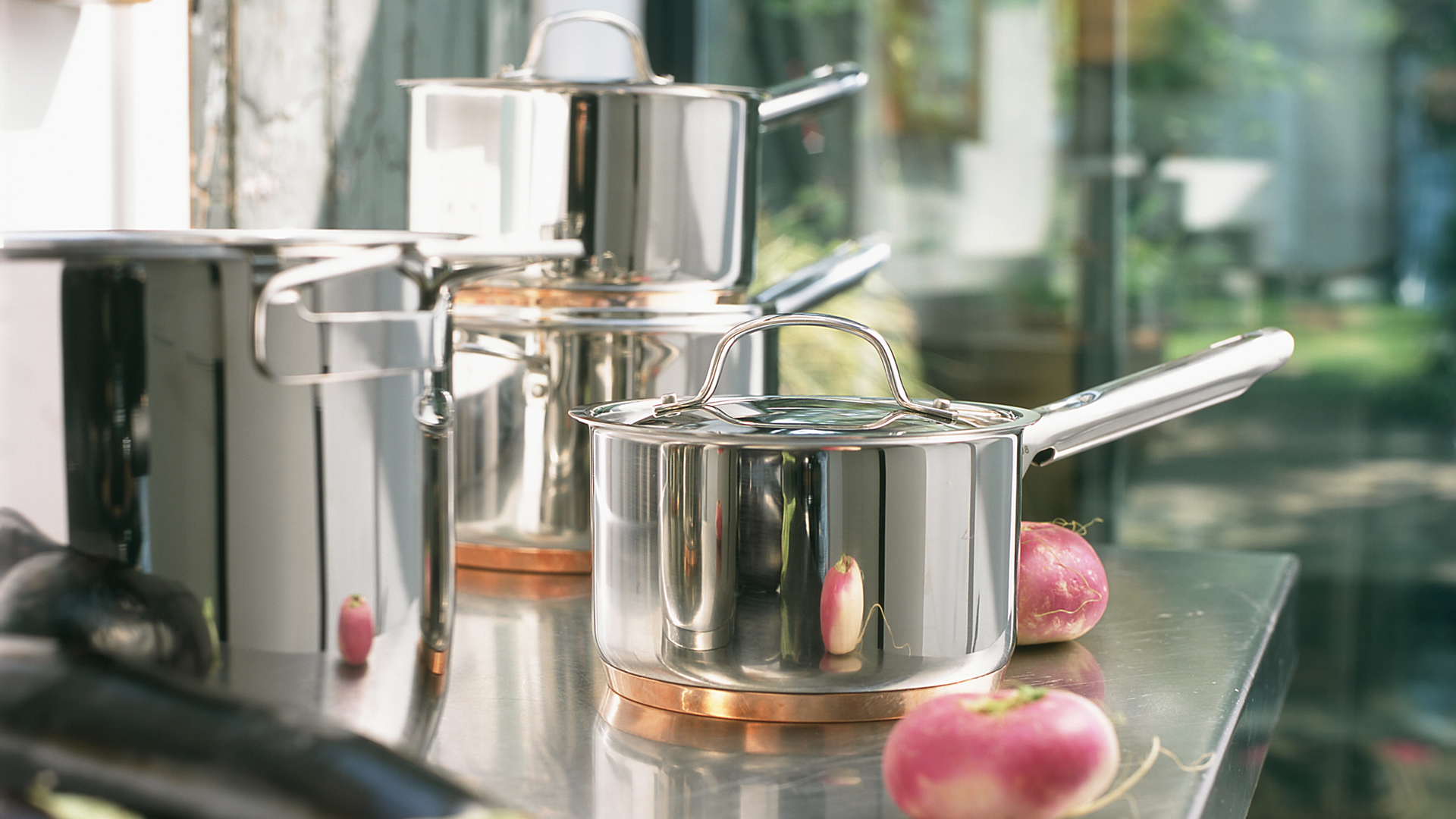 set of stainless steel saucepans on a kitchen counter with a view to a garden beyond