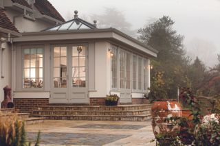 a grey and white orangery by Westbury Garden Rooms, backing onto a large paved patio area of the garden