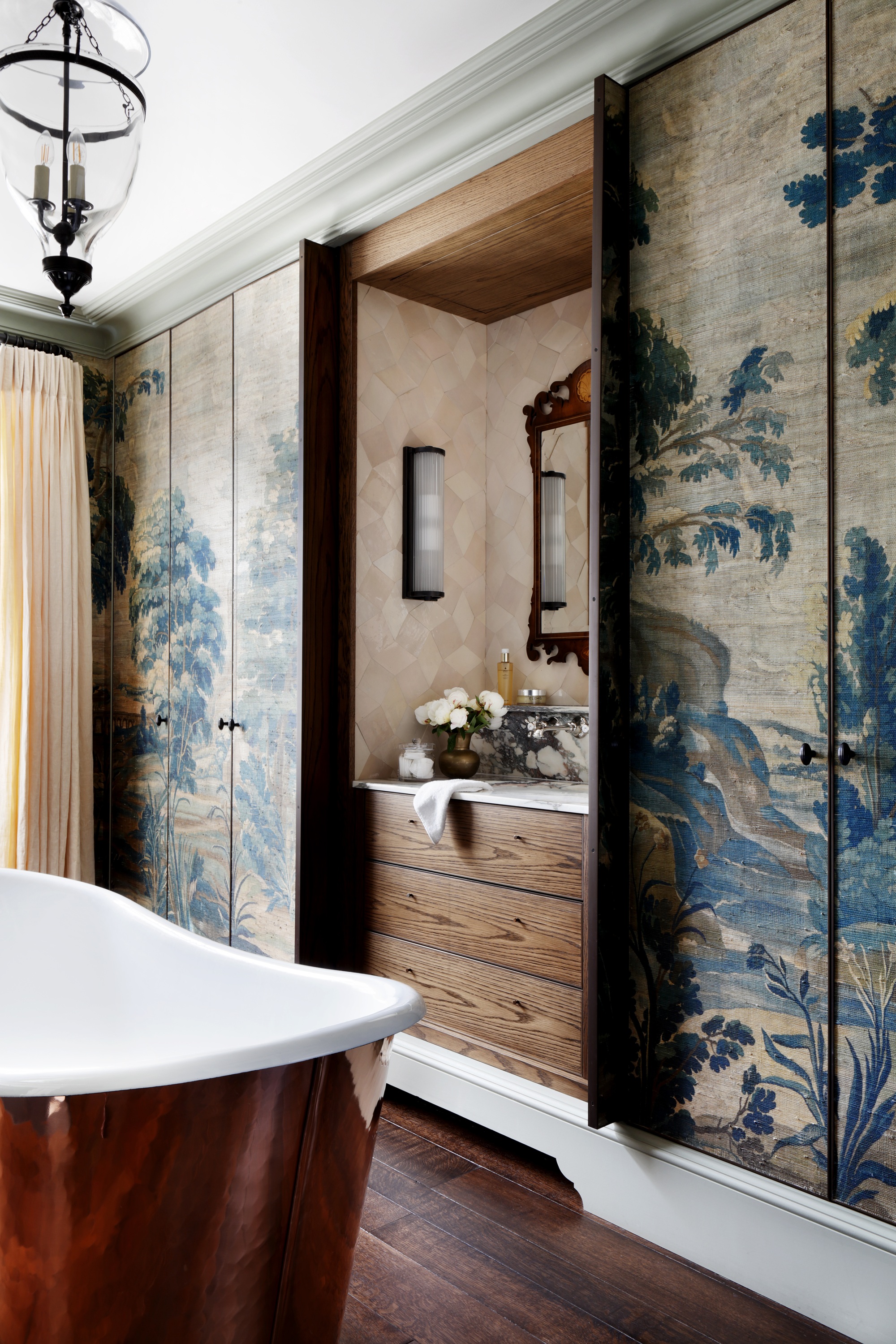 a bathroom with a wooden vanity unit built in behind pocket doors clad in tapestry. a copper bath is in the foreground