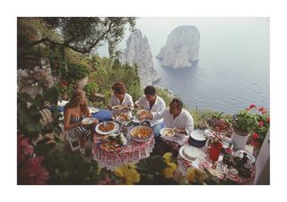 Italian artist and actress Domiziana Giordano, Italian author Francesca Sanvitale, Dino Trappetti and Umberto Terrelli dining al fresco on a terrace overlooking the waters off the coast of the island of Capri, Italy, in August 1980.