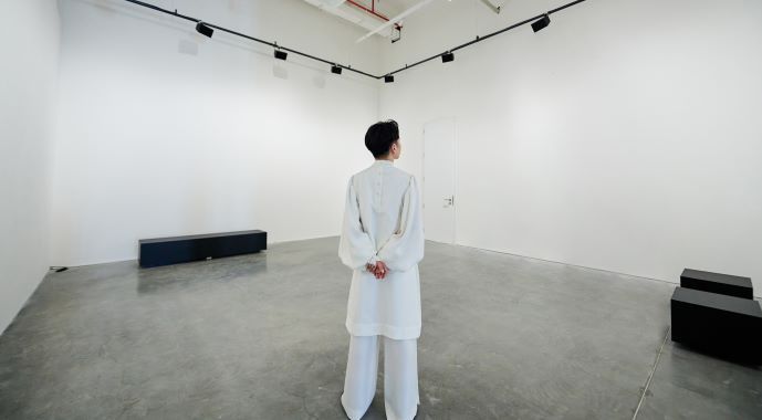 Phạm Minh Hiếu stands and looks at his all-white art space brought to light with d&amp;b Soundscape.