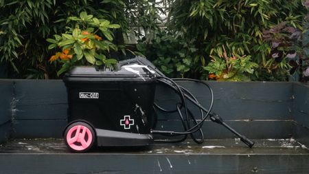 Side view of the Muc-Off Mobile Bike Pressure Washer with lance and hose on a grey bench