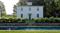 a traditional white feather boarded carriage house surrounded by hydrangeas and a pond