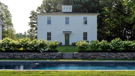 a traditional white feather boarded carriage house surrounded by hydrangeas and a pond