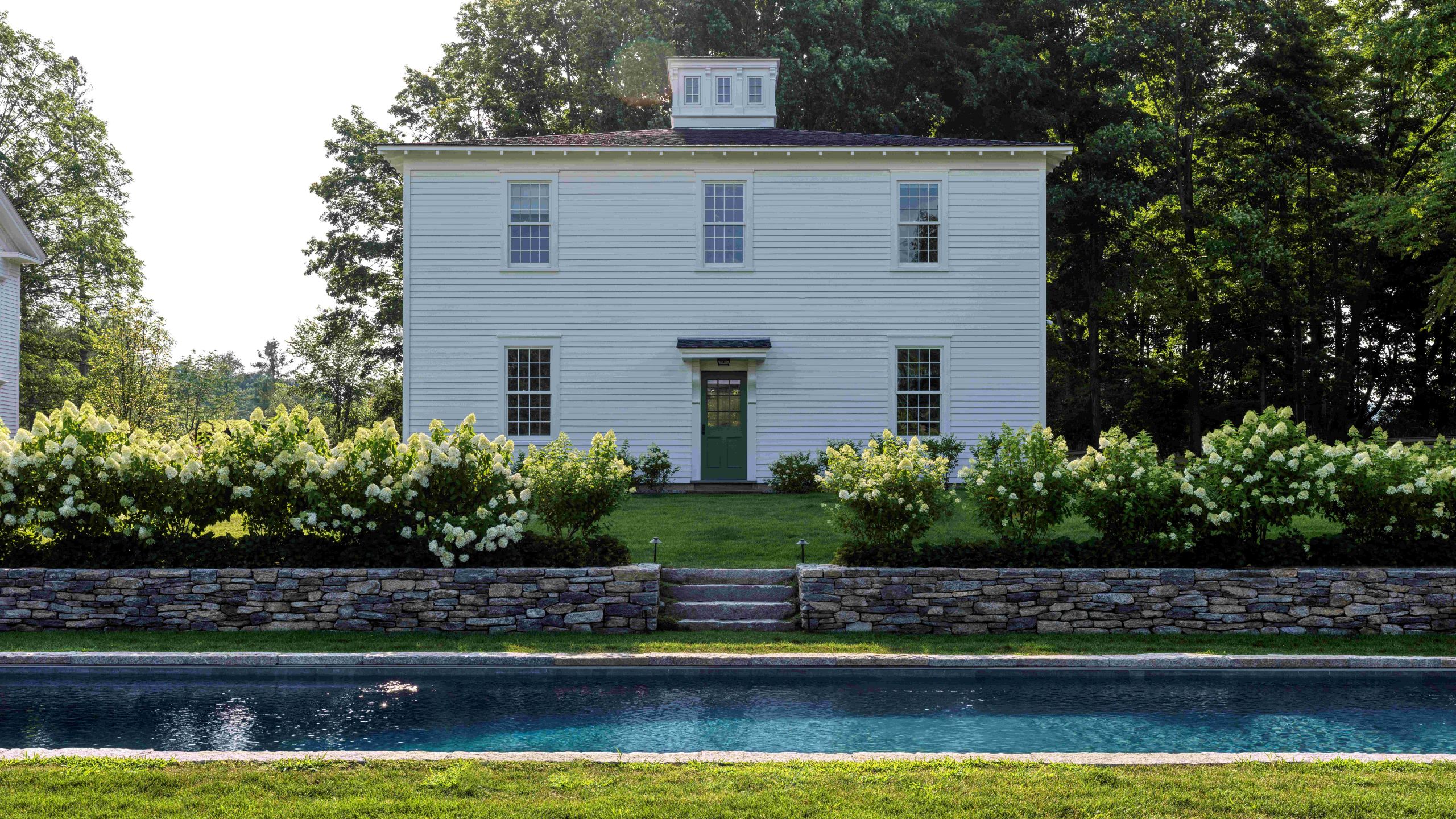 a traditional white feather boarded carriage house surrounded by hydrangeas and a pond