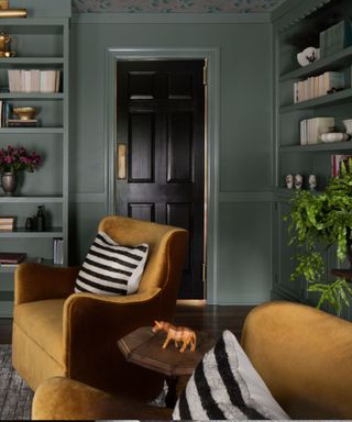 A green library with gold armchairs and a black rustic door