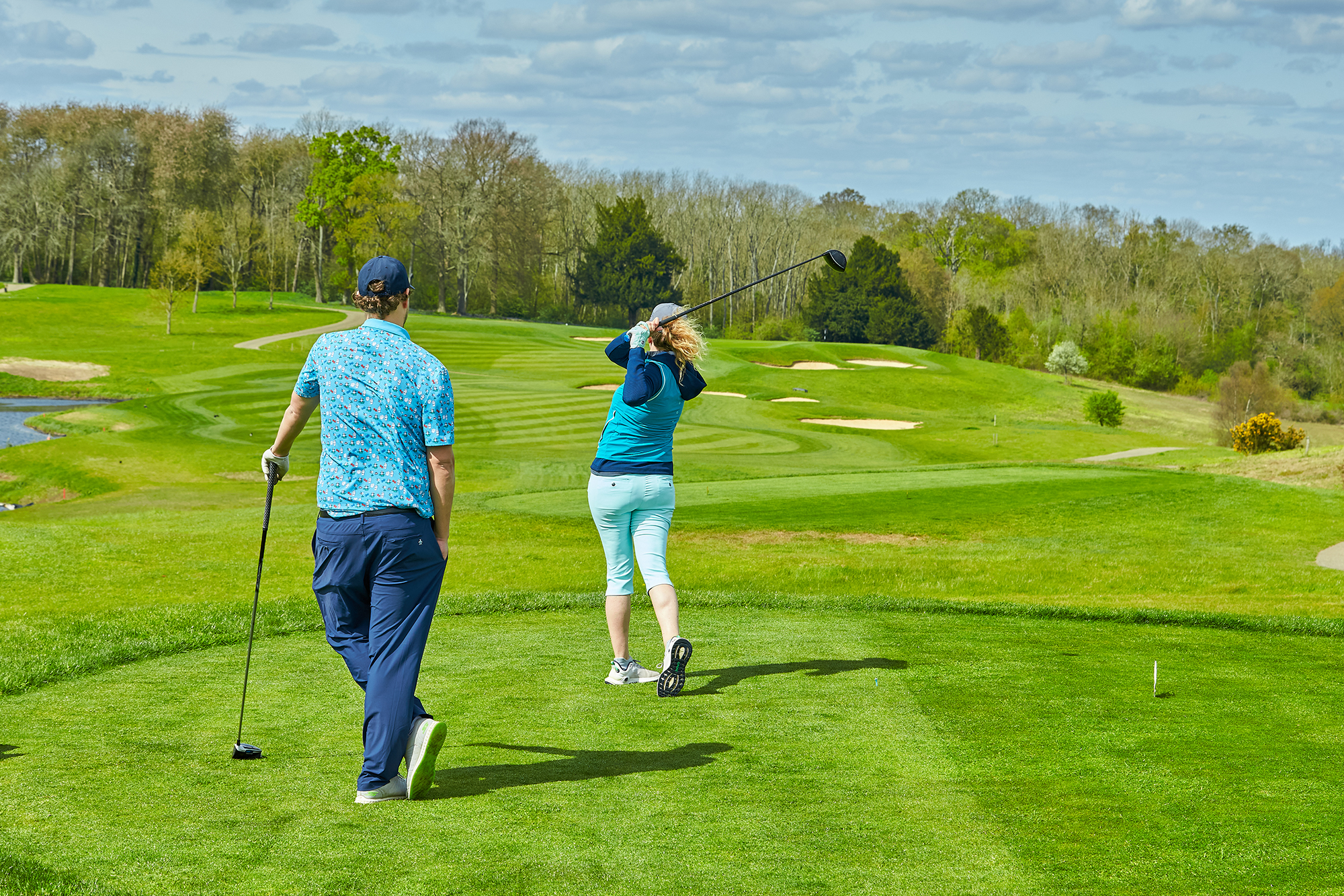 A golfer hitting a tee shot in front of their playing partner as they play ready golf to speed up pace of play
