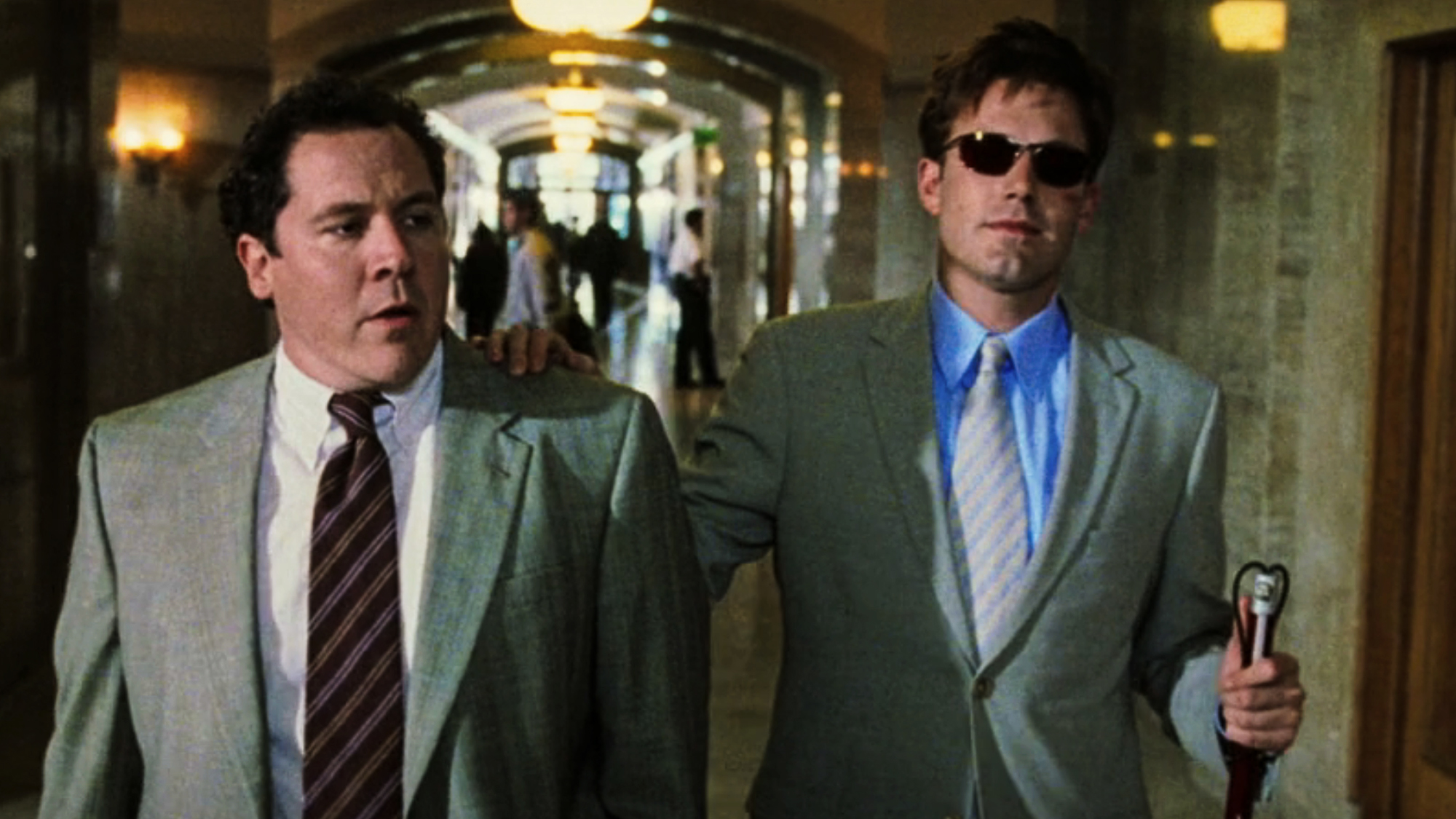 Ben Affleck and Jon Favreau wearing suits and ties walking down a courthouse hallway in Daredevil (2003).