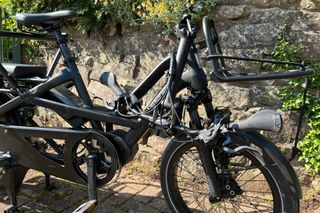 The Tern GSD range of electric cargo bikes can have it's handle bars folded to the side for space saving like to one in the image, which has a stone wall and greenery in the background.