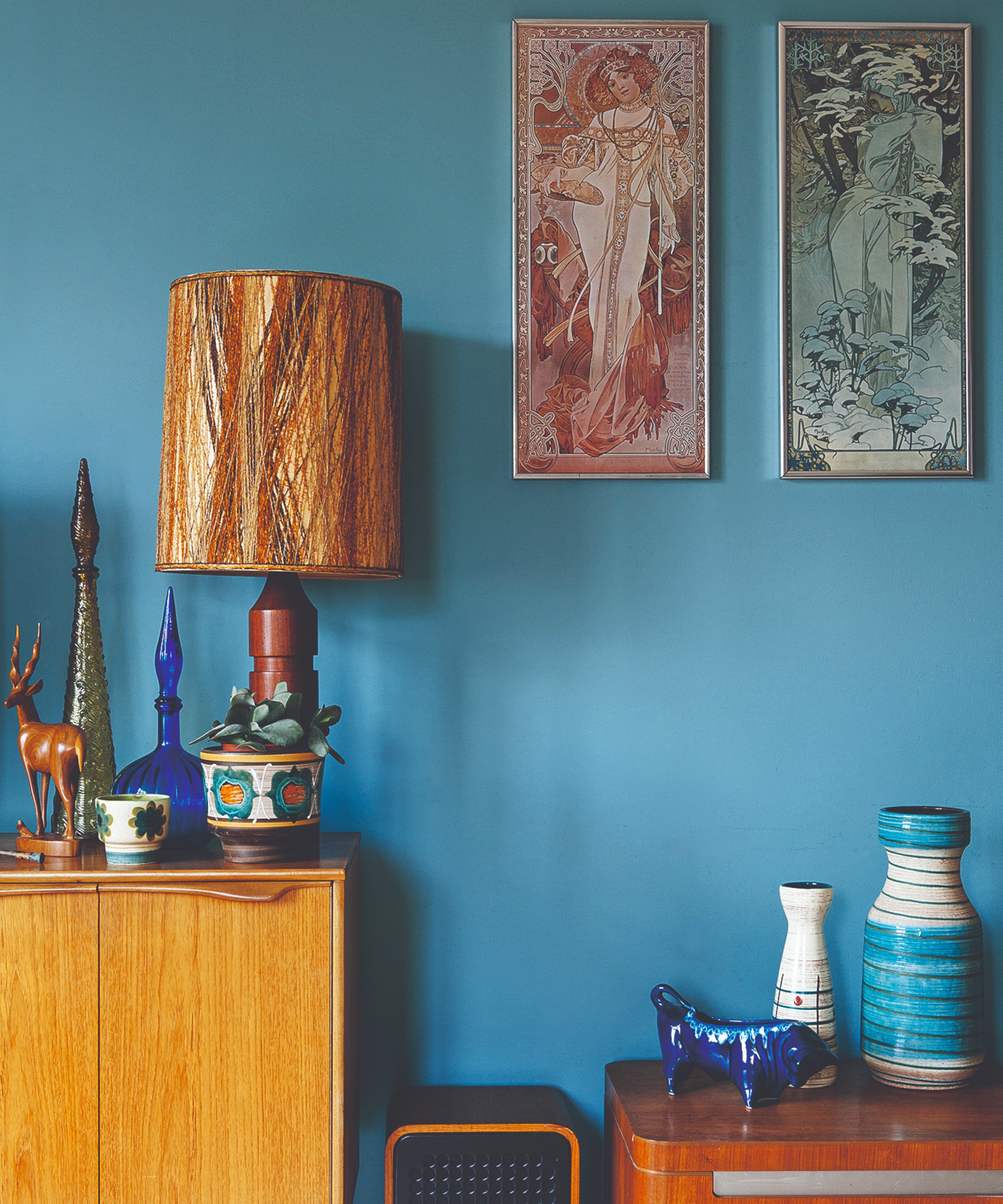 A blue-painted living room with a mid-century sideboard and art deco art prints hung on the wall