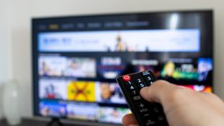 A hand holding a remote browsing streaming service on television