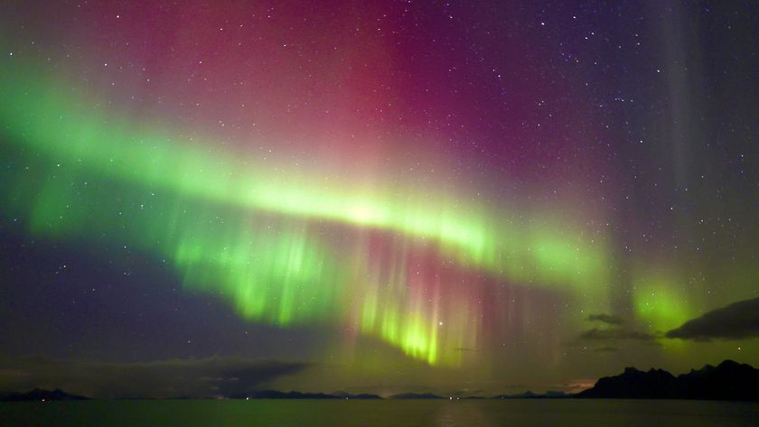 northern lights in the sky and reflecting in the water below. they appear as green and magenta ribbons of light stretching across the sky.